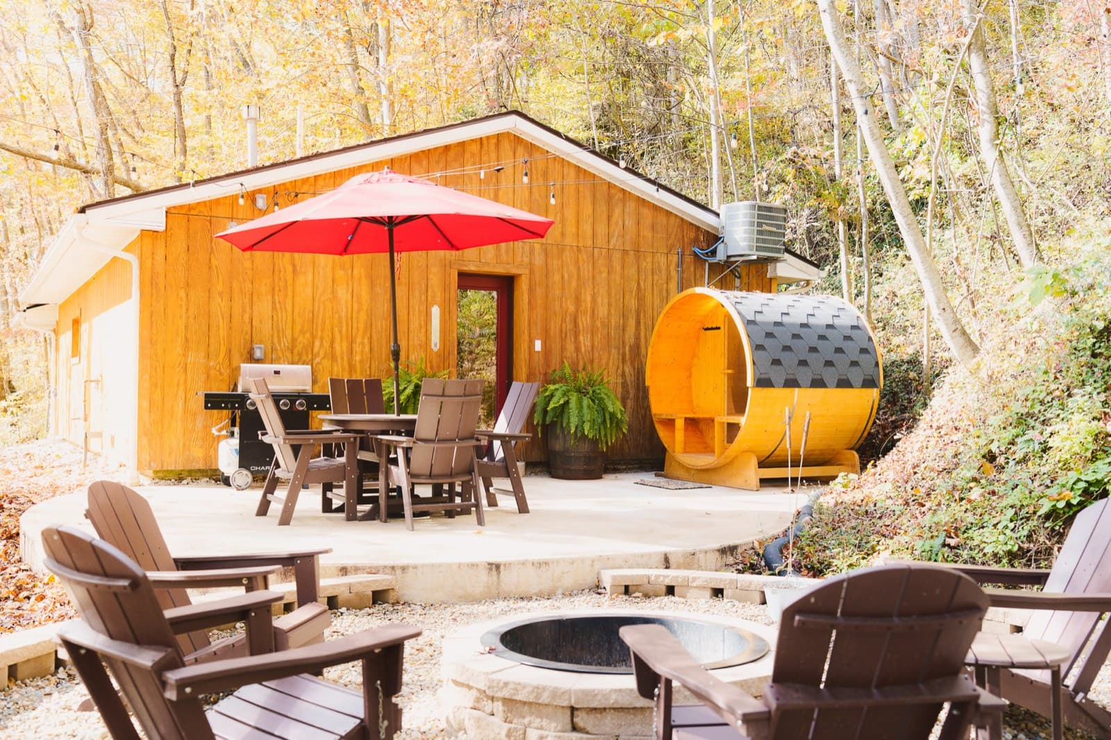 A cabin patio with a barrel sauna, fire pit, and dining set