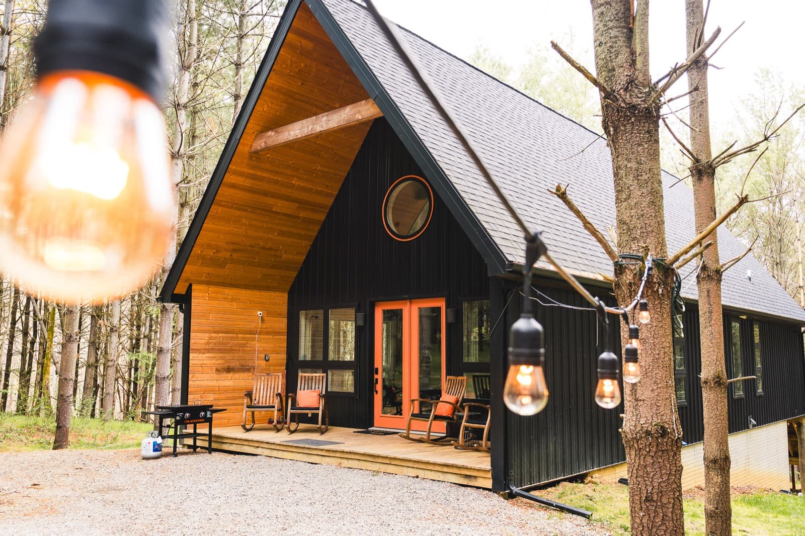 A black A-frame cabin framed by string lights in the pines